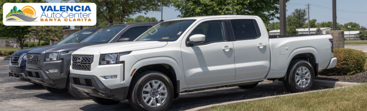 Row of new trucks for sale at Valencia Auto Center under clear Santa Clarita skies.